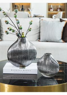 two silver vases sitting on top of a table next to a white couch in a living room