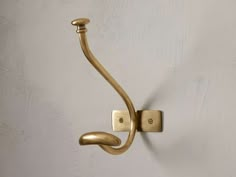 a gold hook on a white wall with a light in the corner and one arm extended