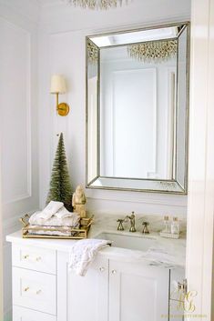 a white bathroom with a christmas tree on the sink counter and mirror above it,