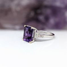 This Deep Purple Amethyst Ring is an elegant and timeless accessory crafted in solid 14k white gold. The emerald cut 10x8mm center stone is highlighted by sparkling baguette diamond accents. Perfect for February birthdays or to make a statement. Elegant Octagon Amethyst Ring For Formal Occasions, Elegant Asscher Cut Purple Ring, Elegant Purple Asscher-cut Ring, Elegant Purple Asscher Cut Ring, Elegant Amethyst Octagon Ring, Elegant Rectangular Amethyst Ring For Formal Occasions, Elegant Octagon Amethyst Rings, Classic Emerald Cut Purple Rings, Classic Purple Emerald Cut Rings