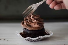 a person cutting into a chocolate cupcake with a fork