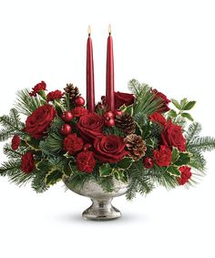 a christmas centerpiece with red roses, pine cones and candles in a silver bowl