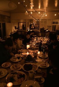 a group of people sitting at a table with plates of food and candles in front of them