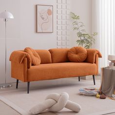 an orange couch sitting on top of a white rug in a living room next to a lamp