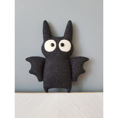 a black bat stuffed animal sitting on top of a white table next to a gray wall