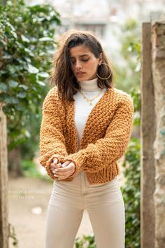 a woman in white pants and a yellow cardigan sweater is standing outside with her arms crossed