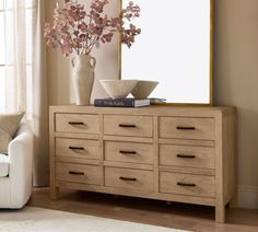 a vase with flowers on top of a dresser next to a mirror and couch in a living room