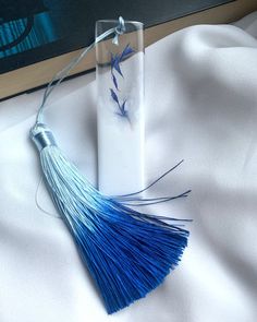 a blue and white tasseled necklace sitting on top of a bed next to a book