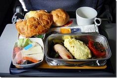 an airplane tray with bread, vegetables and other food items on the tray in front of it