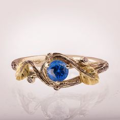 "A delicate, handmade engagement ring made in two gold colors and set with a natural blue sapphire of high quality. The grooves in the band are plated with black rhodium which emphasizes the texture. if you prefer not to apply the black rhodium that is fine. I can also use white, rose, or yellow gold for the band and the leaves for the same price. The ring in the pictures is set with a 4.5mm sapphire but can be set with any other stone, please contact me for a quote. On each side of the ring a small, natural white diamond is set in a 'berry' -----> A Video is Available here - https://youtu.be/OLrUkNPnh5E ---> A matching band is available here - https://www.etsy.com/il-en/listing/656071340/ Please note that sapphires are natural stones and the shade may vary. If you are looking at this ring Unique Yellow Gold Sapphire Ring, Gold Hand Forged Sapphire Ring, Handmade Yellow Gold Sapphire Ring, Hand Forged Gold Sapphire Ring, Hand Forged Blue Sapphire Ring For Anniversary, Hand Forged Blue Sapphire Ring Gift, Anniversary Blue Hand Forged Sapphire Ring, Blue Hand Forged Rings For Anniversary, Hand Forged Blue Rings For Anniversary