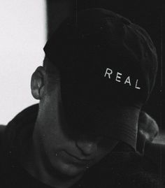 a black and white photo of a man wearing a hat with the word real written on it