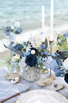 the table is set with blue flowers and candles on it, along with other decorations