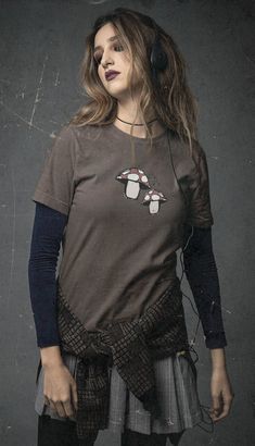 a woman with headphones standing in front of a gray wall wearing a penguin t - shirt