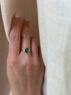 a woman's hand with a green ring on her left wrist and white fabric in the background