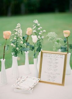 flowers in vases are sitting on a table with a menu and framed photograph next to them