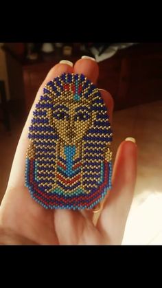 a person is holding a beaded object in their hand and it looks like an egyptian mask