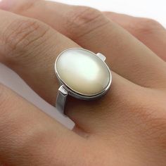 "This is a handmade ring of a large lustrous oval Mother of Pearl. When the stone catches the light it displays a brilliant iridescent glow! The contemporary silhouette of the curved ring band allows the gemstone to truly shine. Available in sizes 5-12. Custom sizing is available upon request!  Dimensions: The hand model is wearing a size 7. The stone measures 16x12mm (about 3/4\" inch). The band is 3mm wide, and the entire face of ring is 17mm, or almost 3/4\" inches. The bezel around the stone Oval Cabochon Opal Ring With Polished Finish, White Oval Opal Ring With Polished Finish, Modern Oval Moonstone Ring For Weddings, Classic Oval Rings With High Luster, Classic Oval Ring With High Luster, Modern Oval Cabochon Moonstone Ring, Classic Oval High Luster Ring, Modern Oval Moonstone Jewelry, Modern Oval Cabochon Opal Ring As Gift