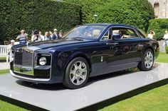 a black rolls royce parked on top of a white platform in front of a crowd