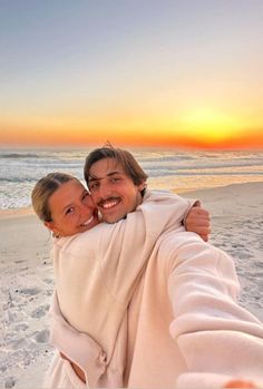 a man and woman taking a selfie on the beach at sunset with their arms around each other