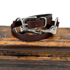 Wrap bracelets are all the rage so we are brought back a classic beauty from Rebecca Ray with a new larger buckle and loop that look fantastic and make it easier to put on yourself. This simple loose ring snaffle bit is the focal point of this triple wrap genuine bridle leather bracelet. A full 2" of adjustment can be made with the authentic bridle buckle for a perfect fit for most any wrist size. Full bracelet length is 25" tip to tip. 1/2" wide bracelet strap. Size adjustment is 21" (Small) to Classic Adjustable Jewelry With Silver Buckle, Adjustable Brown Leather Bracelet With Custom Hardware, Adjustable Brown Leather Bracelet With Belt Detail, Adjustable Leather Bracelet With Custom Hardware, Adjustable Leather Bracelet With Custom Hardware As Gift, Classic Adjustable Double Band Leather Bracelet, Adjustable Brown Leather Belt Bracelet, Adjustable Brown Jewelry With Antique Buckle, Red Leather Bracelet