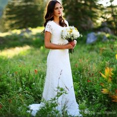 a woman in a white dress holding flowers and looking off into the distance with trees in the background