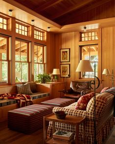 a living room with wood paneling and lots of pillows on the couches in front of large windows