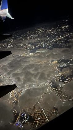 an airplane wing flying over the city lights and clouds at night in the dark sky