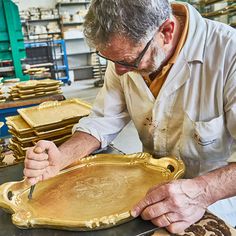 a man working on gold trays in a shop