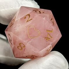 a pink and gold dice sitting on top of someone's white gloved hand