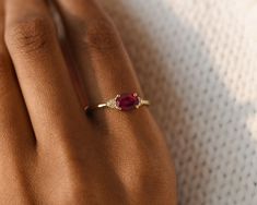 a woman's hand wearing a gold ring with a red stone in the middle