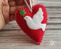 someone is holding a heart shaped ornament with a white dove on it and green leaves