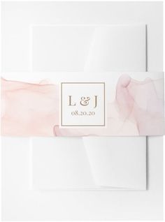 a white envelope with a pink and gold foiled logo on the front, along with a card that reads l & j