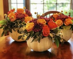 two white pumpkins filled with flowers sitting on top of a wooden dining room table