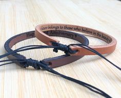 three leather bracelets with words on them sitting on a wooden table next to each other