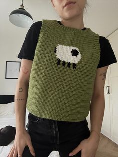 a woman standing in front of a bed wearing a green sweater with sheep on it