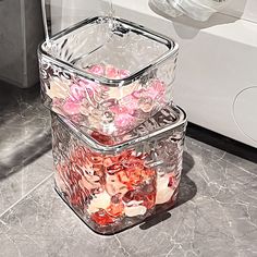 two clear containers filled with pink and white flowers on top of a marble floor next to a washing machine