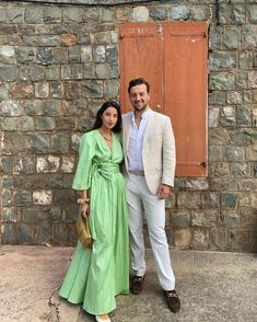 a man and woman standing next to each other in front of a stone building with wooden doors