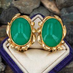 This great pair of cabochon earrings are each bezel set with one oval cabochon cut chrysocolla that is accented with a ribbon motif border. The earrings are crafted in 14k yellow gold and are finished with omega backs for pierced ears. Elegant Green Cabochons For Formal Occasion, Elegant Green Cabochons For Gifts, Elegant Green Cabochons As Gifts, Formal Green Oval Cabochon Jewelry, Oval Cabochon Clip-on Earrings Gift, Elegant Green Oval Clip-on Earrings, Cabochon Earrings, Brand Presentation, Ruby Birthstone