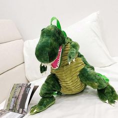 a stuffed dinosaur sitting on top of a bed next to a pillow and magazine holder