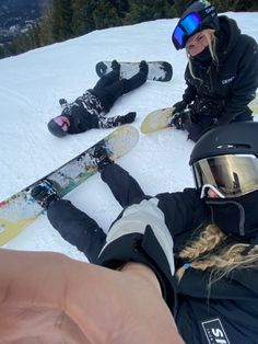 three snowboarders sitting in the snow with their feet up and one person pointing at them