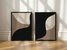 two black and white framed art pieces sitting on top of a wooden floor