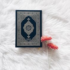 a blue book sitting on top of a fluffy white blanket next to a red flower