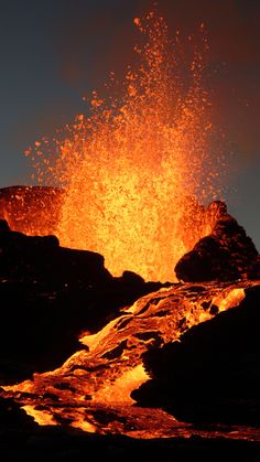 an orange and yellow fire spewing out from the top of a rocky hill