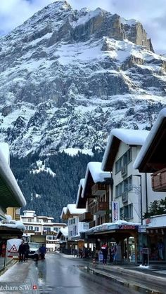 people are walking down the street in front of snow covered mountains and buildings with shops on each side