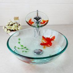 a glass bowl sink with goldfish in it and flowers on the table behind it