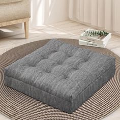 a grey ottoman sitting on top of a rug next to a white book and chair