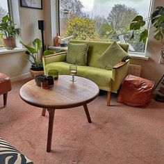 a living room filled with furniture next to a window covered in green plants and potted plants