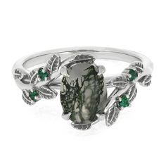 a white gold ring with green stones and leaves on the band, set in silver