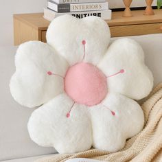 a white flower pillow sitting on top of a couch next to a pile of books