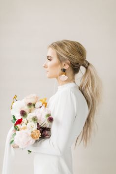 a woman with long hair holding a bouquet of flowers in her hand and wearing earrings